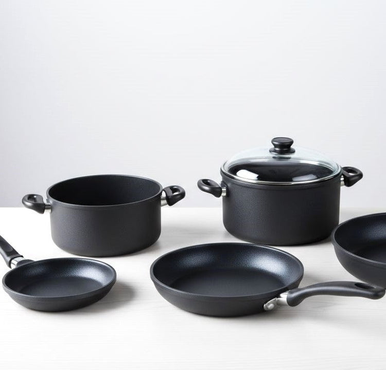 Sortiment aus Aluminiumguss Pfannen und Töpfen in unterschiedlichen Größen auf hellem Holzuntergrund